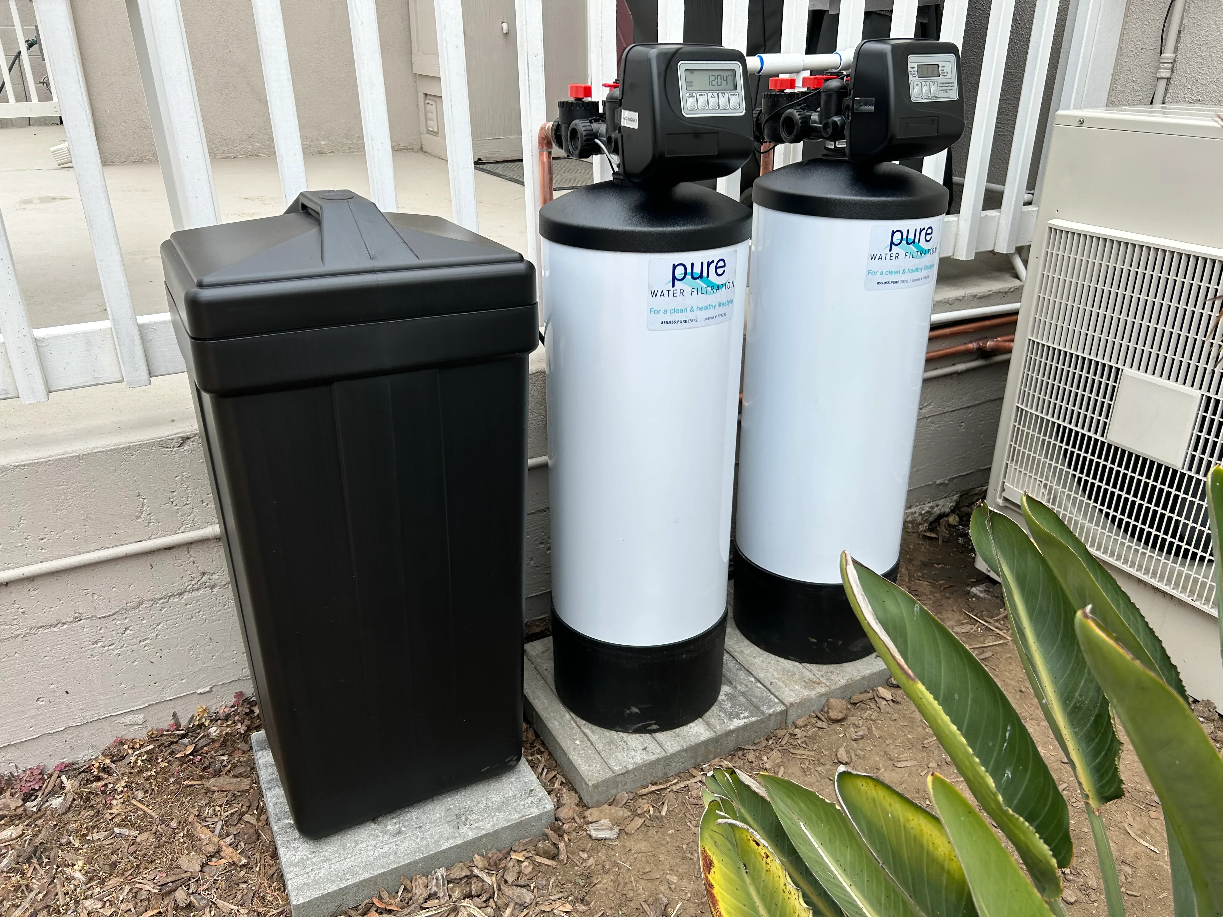 Two white water filtration tanks with digital controls and black resin tank installed on concrete pad