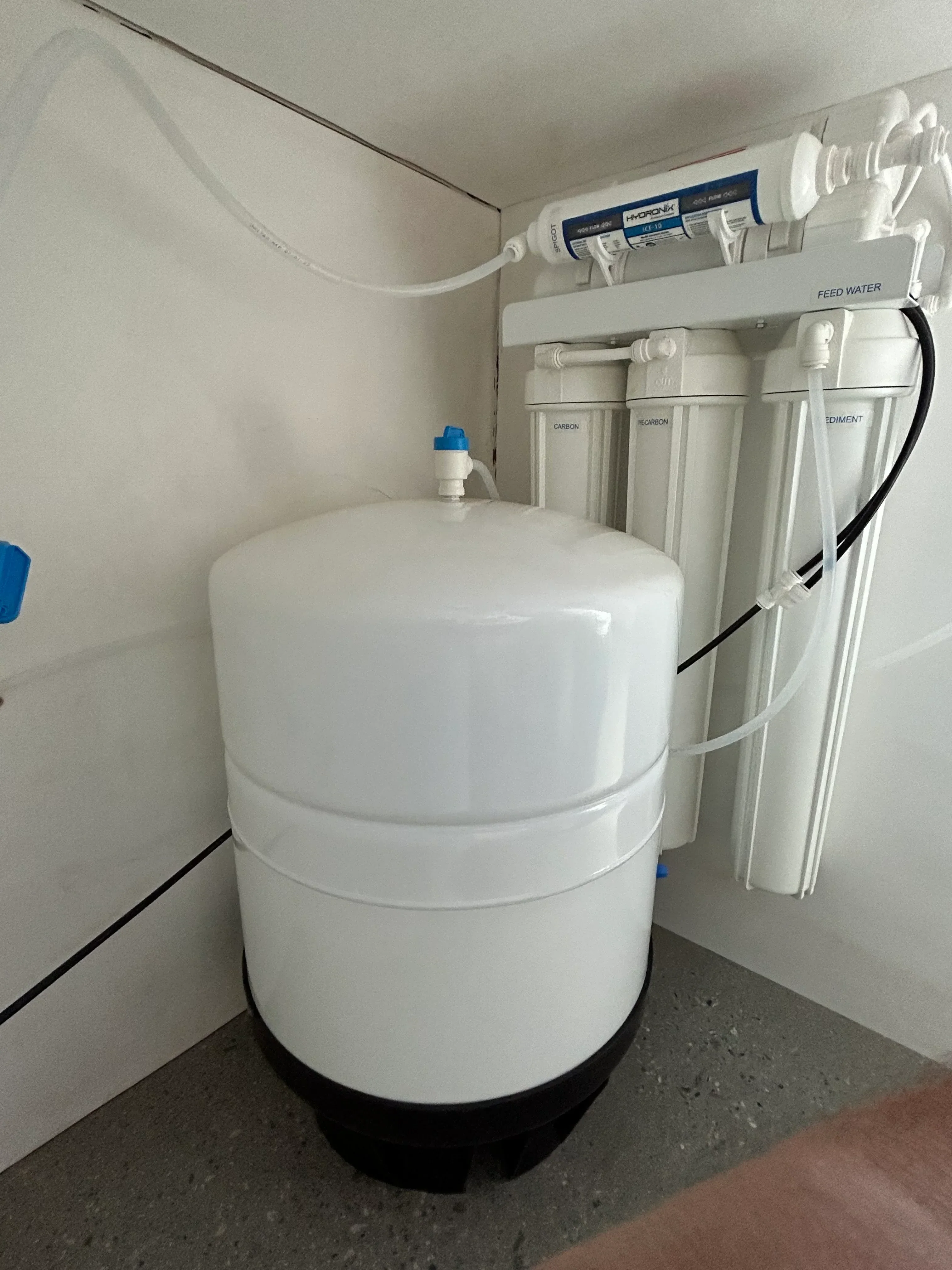 Multi-stage RO system with filter housing, storage tank, and white tubing connections